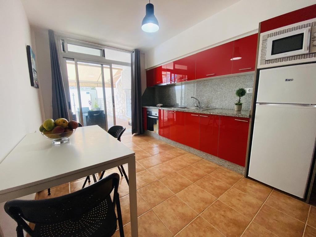 a kitchen with red cabinets and a table with a bowl of fruit on it at VV Ancla in Puerto de Mogán