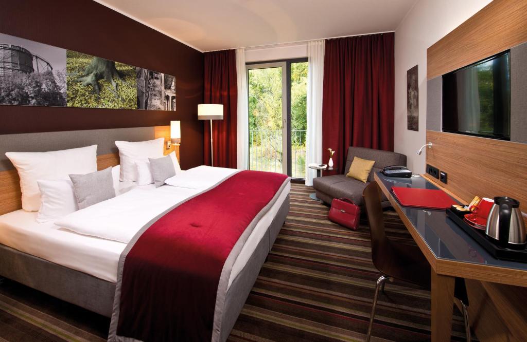 ein Hotelzimmer mit einem großen Bett und einem Schreibtisch in der Unterkunft Leonardo Hotel Völklingen-Saarbrücken in Völklingen