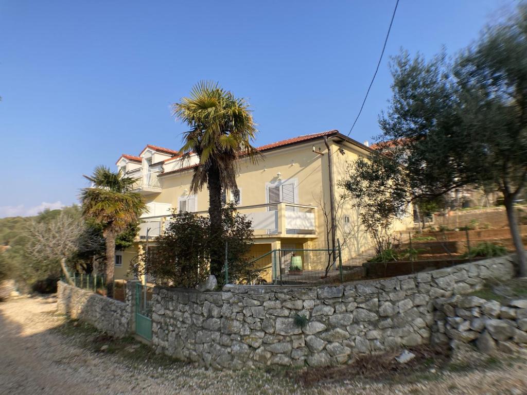 una casa detrás de una pared de piedra con una palmera en Apartments by the sea Lun, Pag - 9395 en Lun