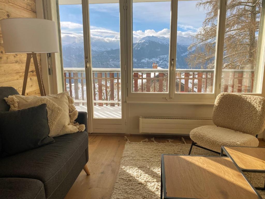 een woonkamer met een bank, een stoel en ramen bij Apartment Del Sol Elysée 4 Crans Montana Switzerland in Crans-Montana