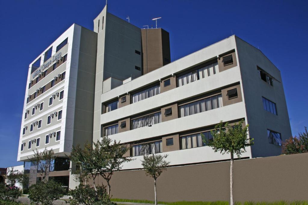 a tall white building with trees in front of it at Hotel Campo Largo Comfort in Campo Largo