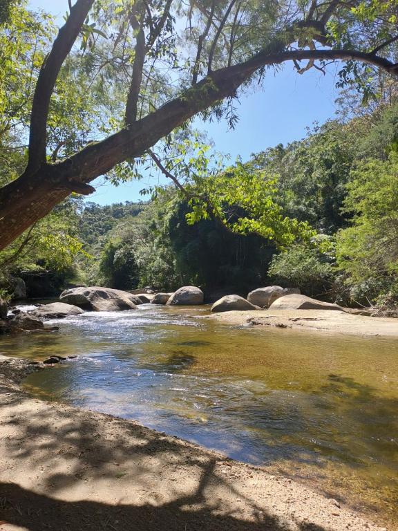 un río con rocas y árboles en el fondo en Lumiar Eco Lodge - Chalé Telhado Verde, en Nova Friburgo