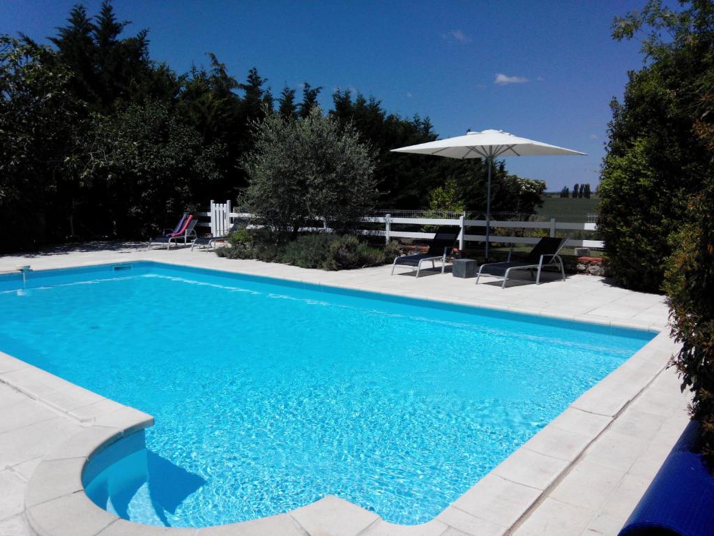a blue swimming pool with an umbrella and chairs at Gites Les Vents Bleus in Donnazac