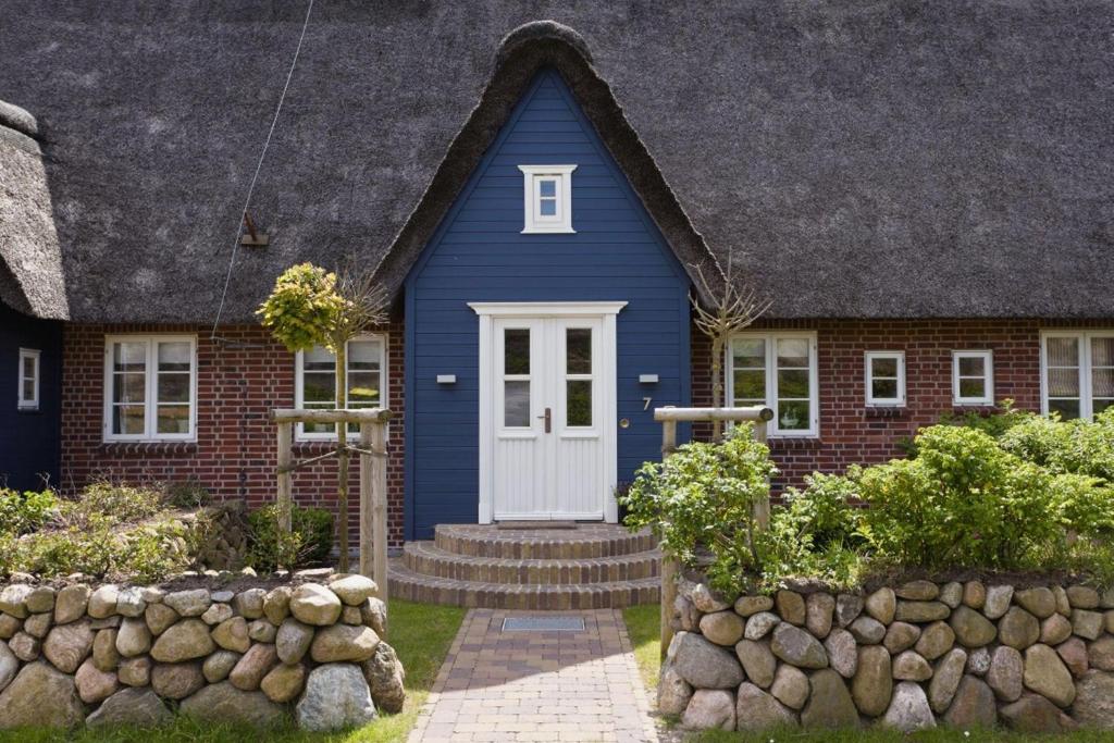 a blue house with a white door and a stone wall at Wattläufer in List