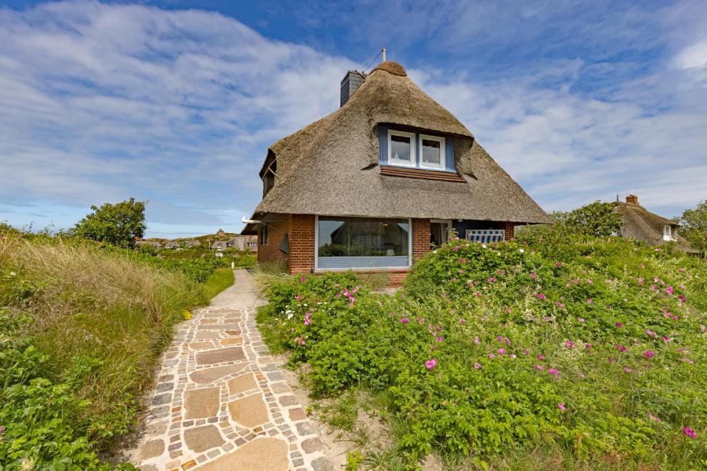 a thatch roof house on a hill with a pathway at Strandhaus in List