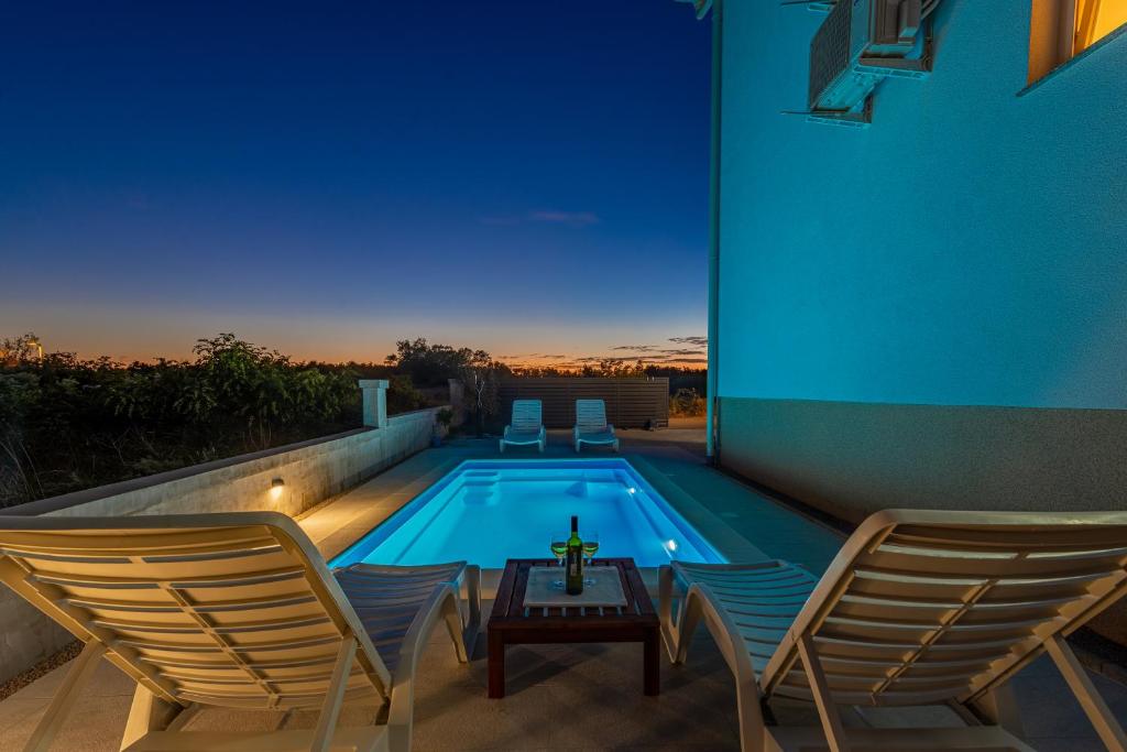 uma piscina com duas cadeiras e uma mesa em frente a uma casa em La Prima Privlaka Luxury Apartments I em Privlaka