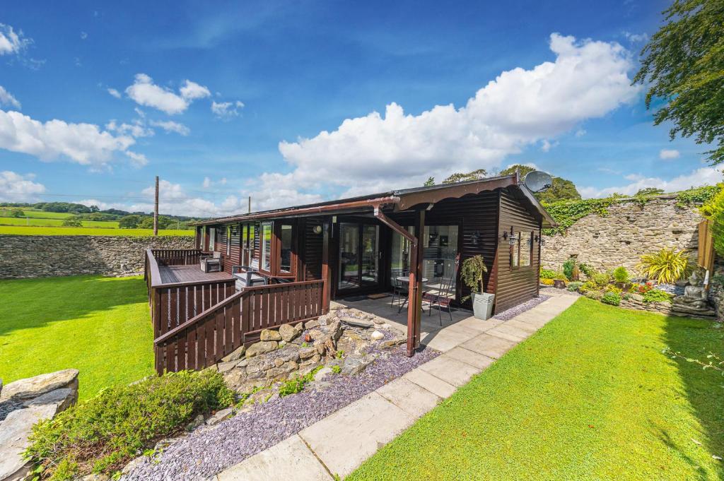 a wooden cabin with a porch and a stone wall at North Lodge Cartmel in Cartmel