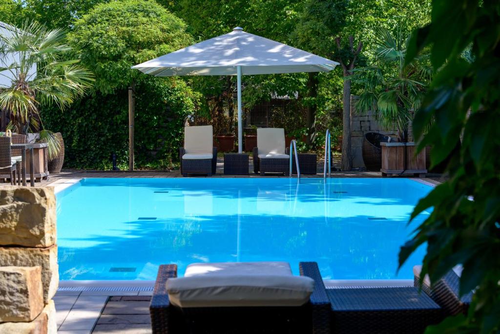 a swimming pool with an umbrella and chairs at Mercure Hotel Hannover Medical Park in Hannover