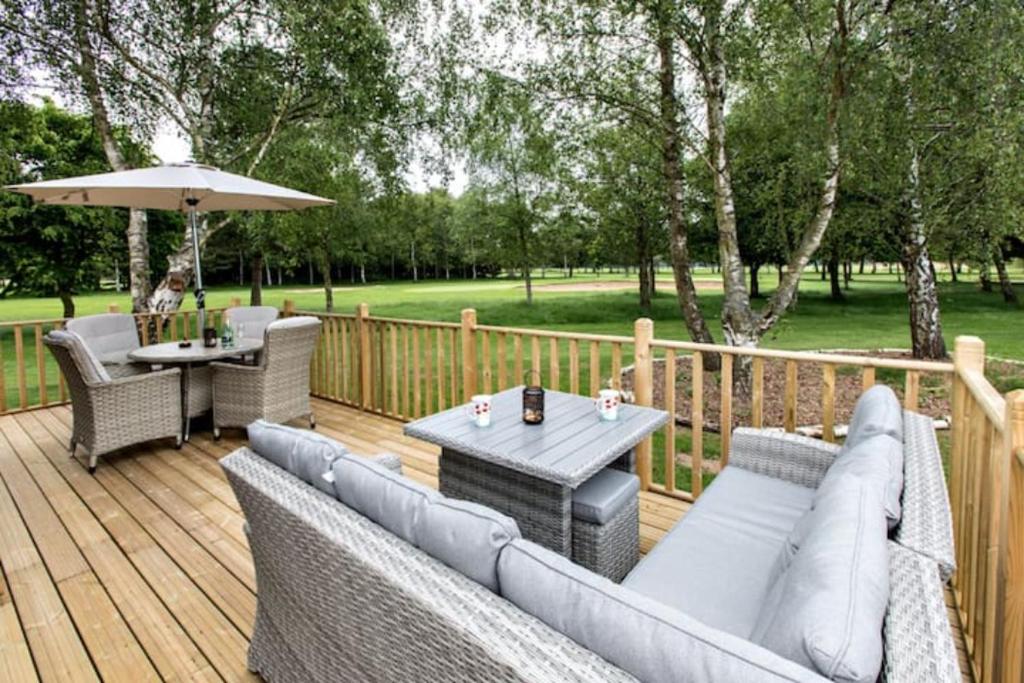 una terraza con sofás, una mesa y una sombrilla en Silver Birches, en Wisbech
