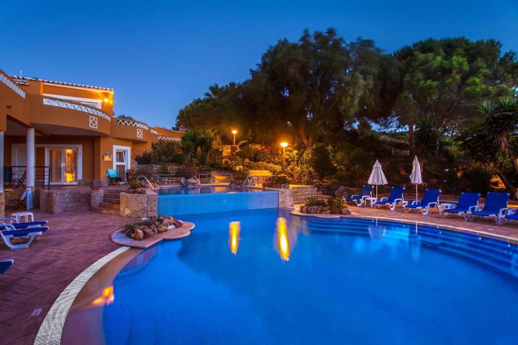 una piscina por la noche con sillas y sombrillas en Montinho De Ouro, en Luz