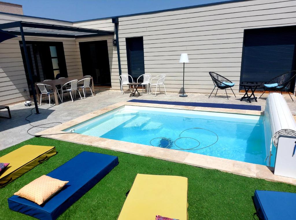 a swimming pool with grass and a patio with chairs at La Belle Vie en Alaric in Douzens