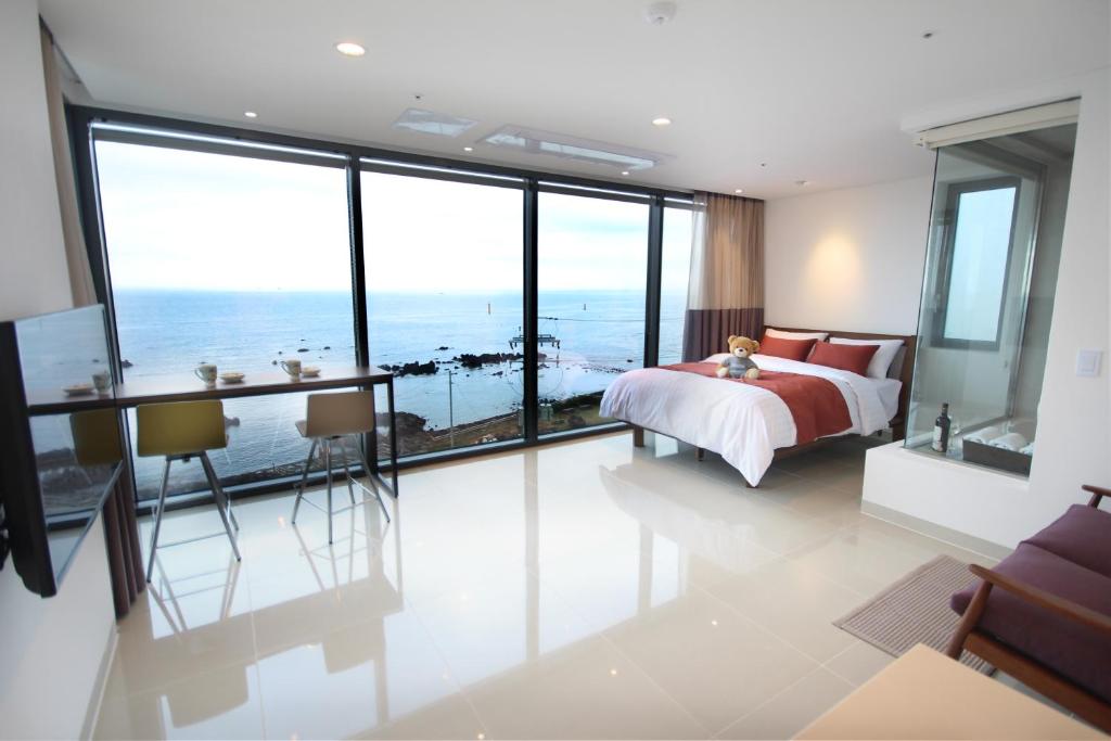 a bedroom with a bed and a desk and large windows at Vista Resort Jeju in Jeju