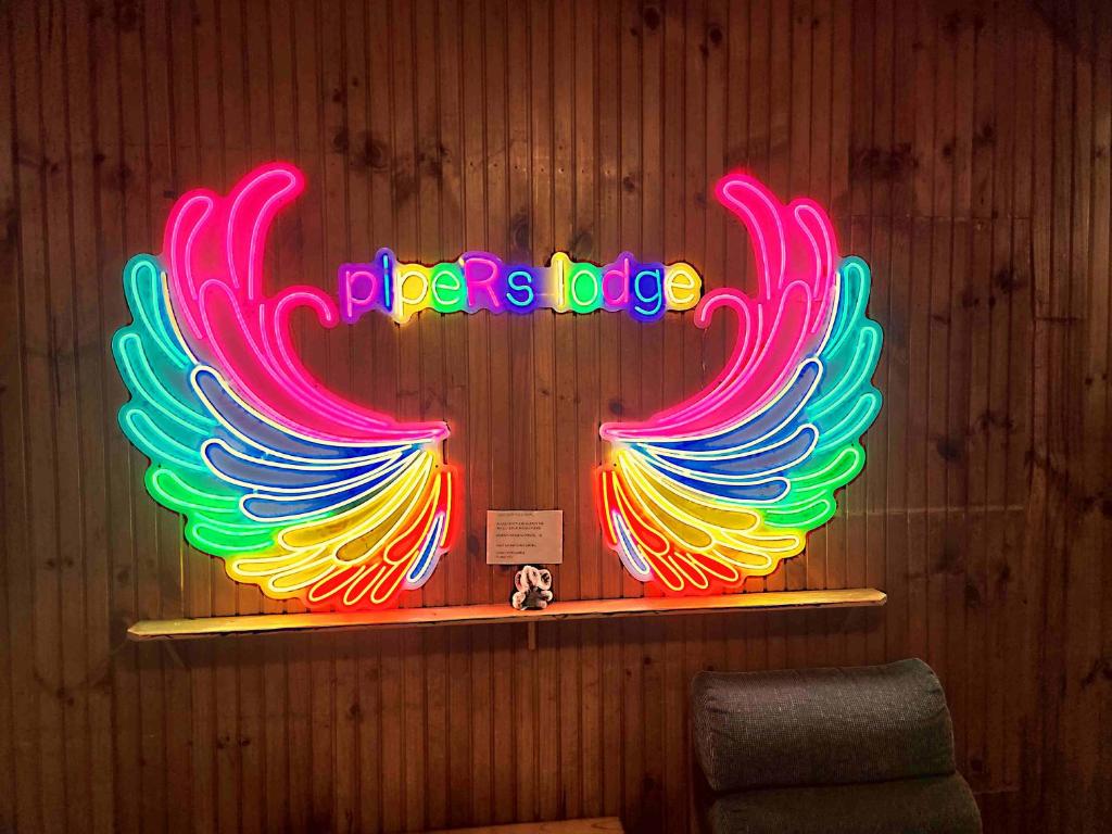 a neon sign with colorful wings on a wooden wall at Pipers Lodge in National Park