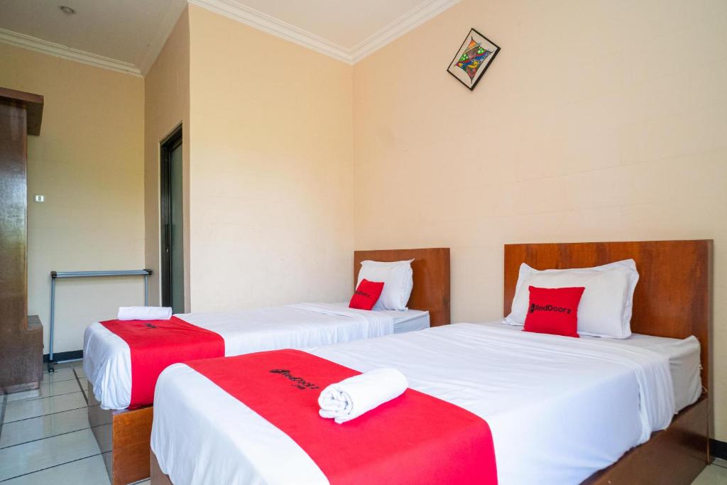 two beds in a room with red and white sheets at RedDoorz Plus Syariah At Lotus Hotel Bojonegoro in Bojonegoro