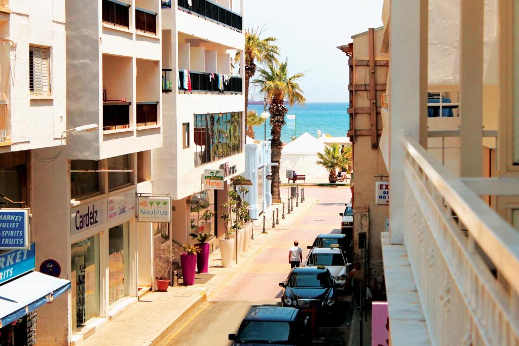 una calle de la ciudad con coches aparcados y el océano en Stephanie City Apartments, en Lárnaca