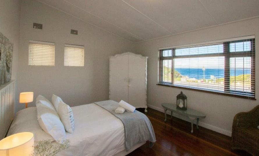 a bedroom with a bed and a table and two windows at Normandie On Sea in Hermanus