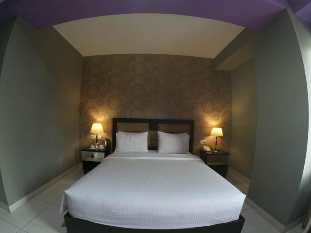 a bedroom with a large white bed with two lamps at Anaya Hotel and Ballroom in Medan