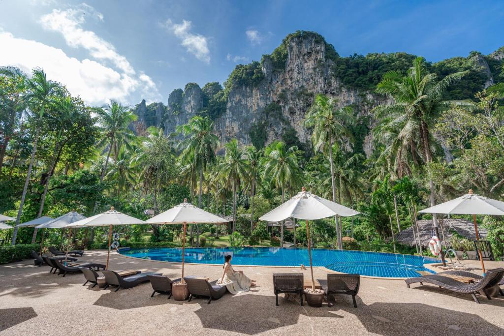 a pool with chairs and umbrellas in front of a mountain at Ban Sainai Resort- SHA Extra Plus Aonang's Green Resort in Ao Nang Beach