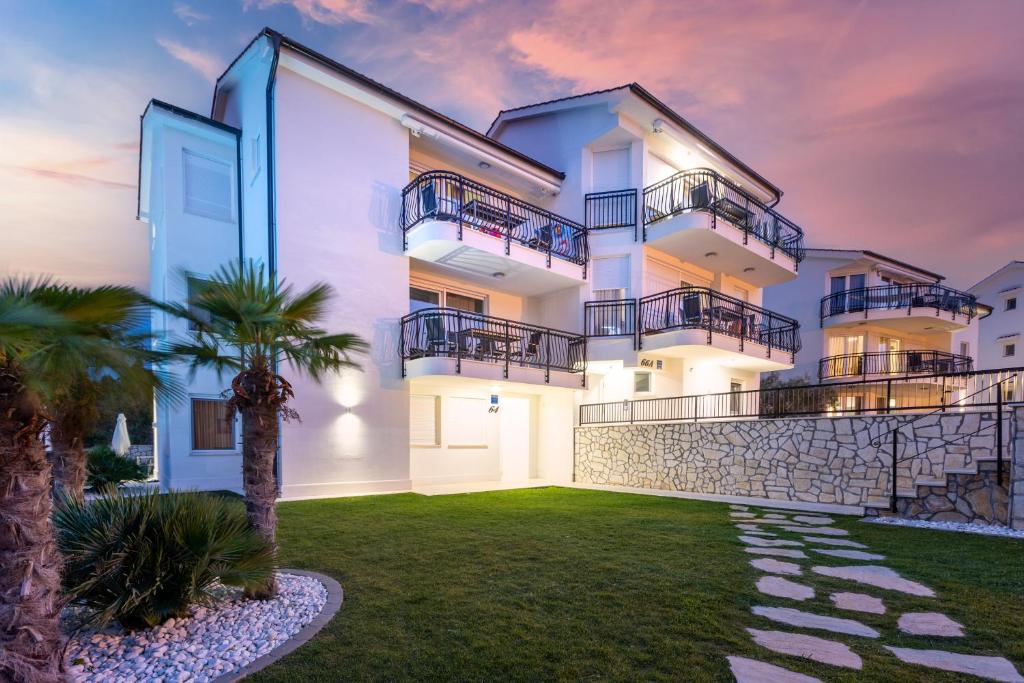 a large white building with balconies and a yard at Cool Šilo Appartement Resort in Šilo
