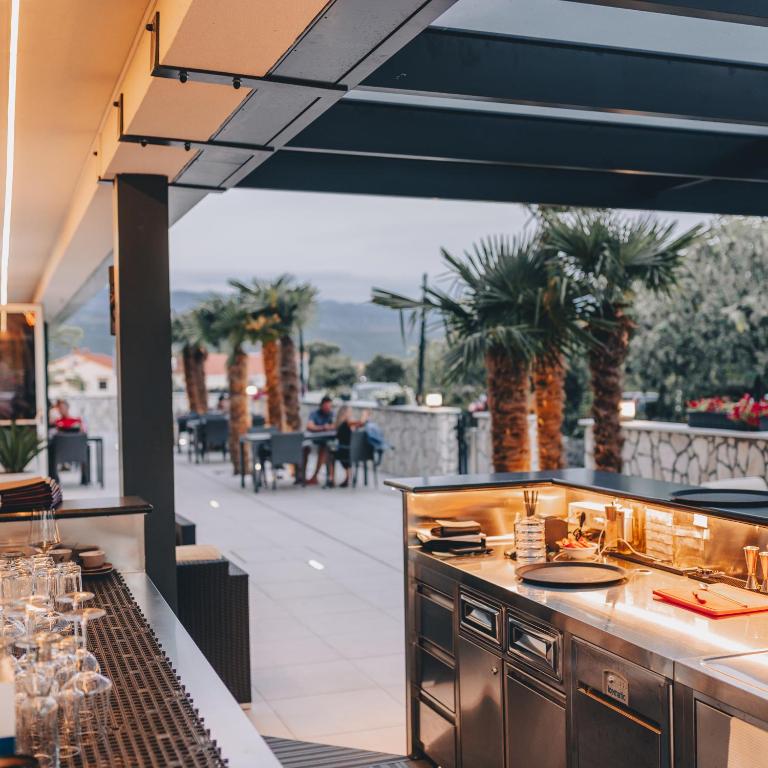 an outdoor kitchen with a bar and a patio at Cool Šilo Appartement Resort in Šilo