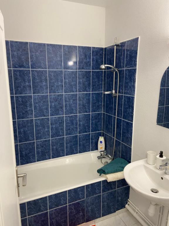 a blue tiled bathroom with a tub and a sink at Bel appartement spacieux, lumineux avec parking in Ris-Orangis