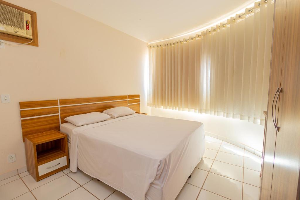 a bedroom with a white bed and a window at Hotel Toulon Caldas Novas in Caldas Novas