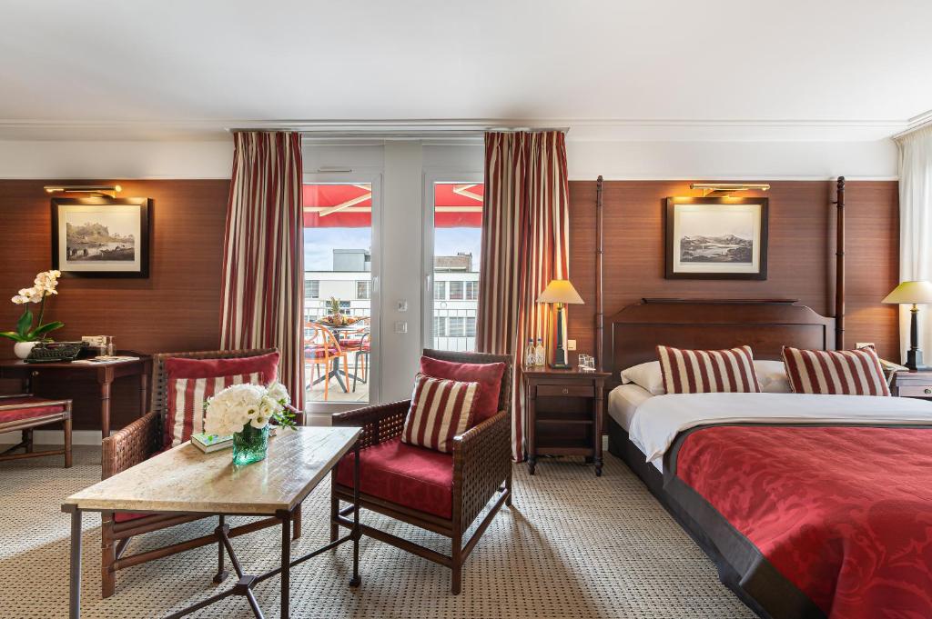 ジュネーヴにあるキプリング マノテルのベッド、テーブル、椅子が備わるホテルルームです。