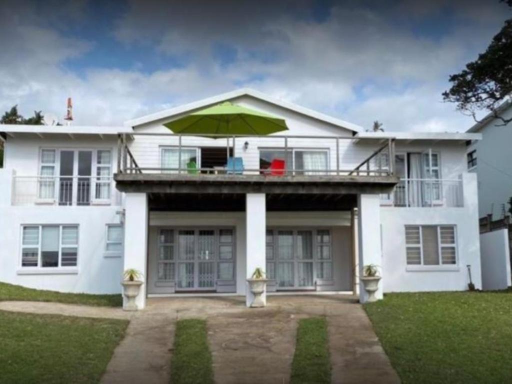 ein weißes Haus mit Balkon und Sonnenschirm in der Unterkunft Umzumbe White House in Umzumbe