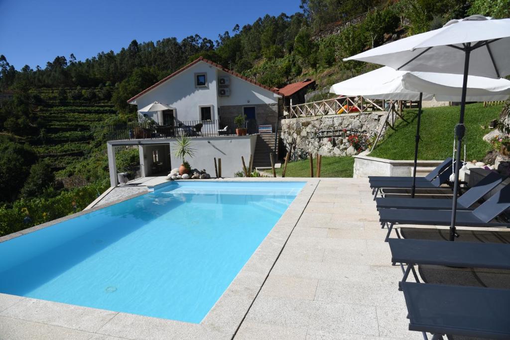 a swimming pool with an umbrella and a house at Casa de Caneiro in Cabeceiras de Basto