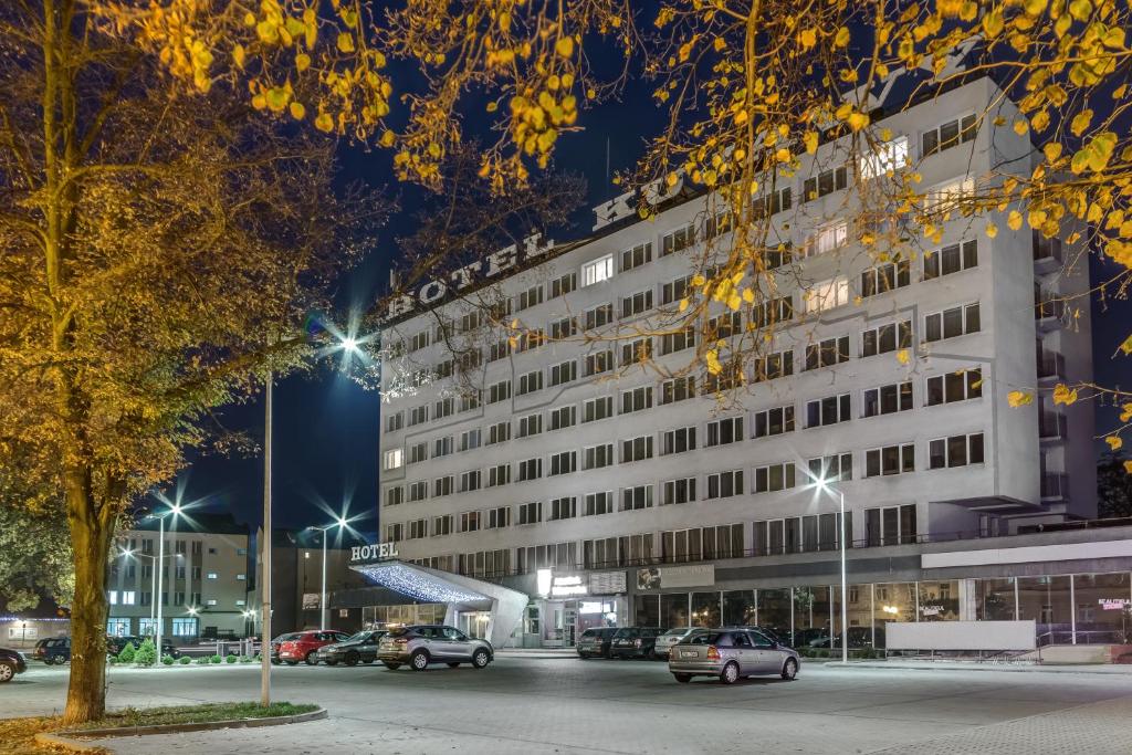 een groot wit gebouw met auto's geparkeerd op een parkeerplaats bij Hotel Kujawy in Włocławek