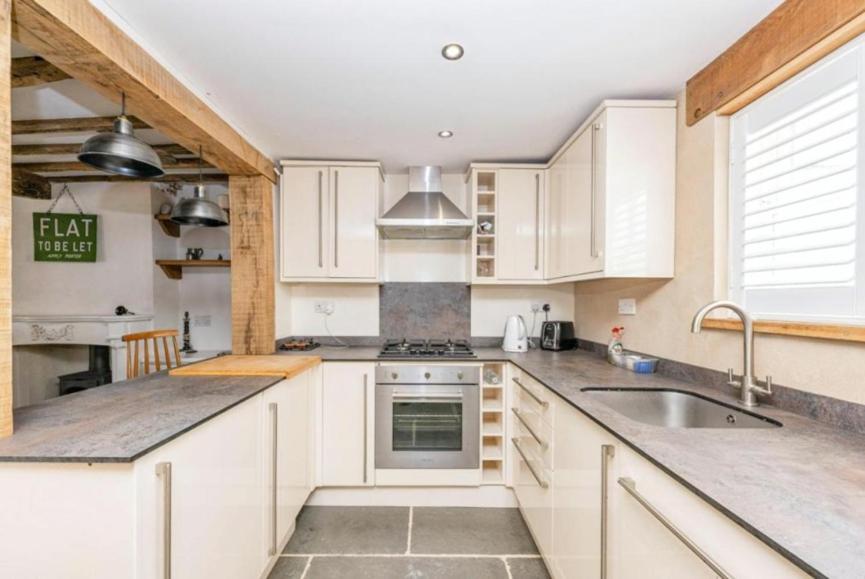 uma cozinha com armários brancos e um lavatório em Samuel Pepys Cottage em Huntingdon