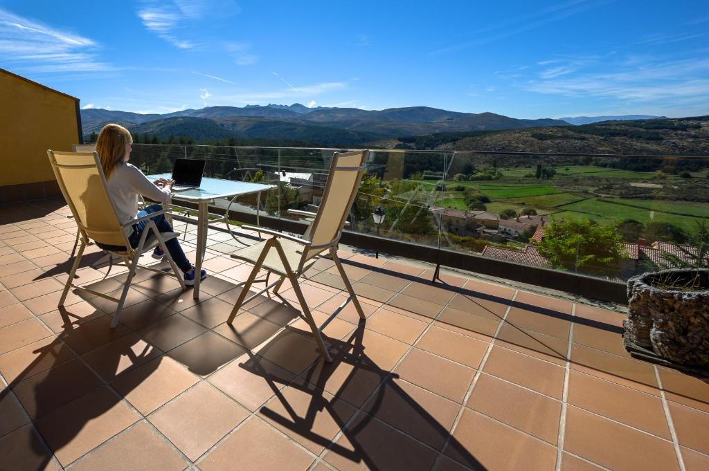 una donna seduta a un tavolo con un computer portatile sul balcone di La Portilla de Gredos. Casa rural a Hoyos del Espino
