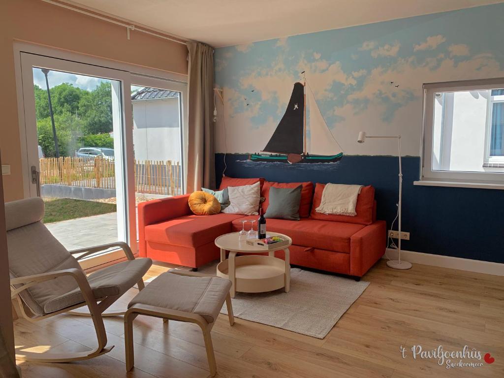 't Paviljoenhûs bij Sneekermeer في Offingawier: غرفة معيشة مع أريكة حمراء وقارب شراعي على الحائط