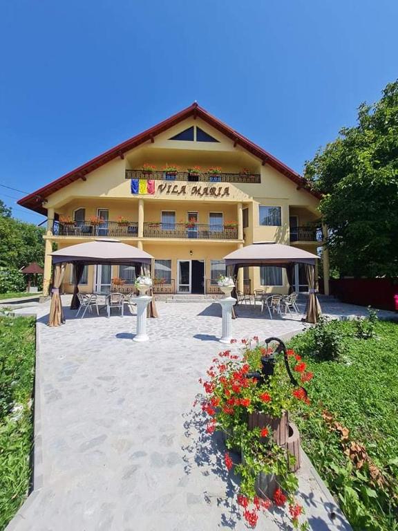 a hotel with tables and umbrellas in front of it at Pensiunea Vila Maria in Crăcăoani