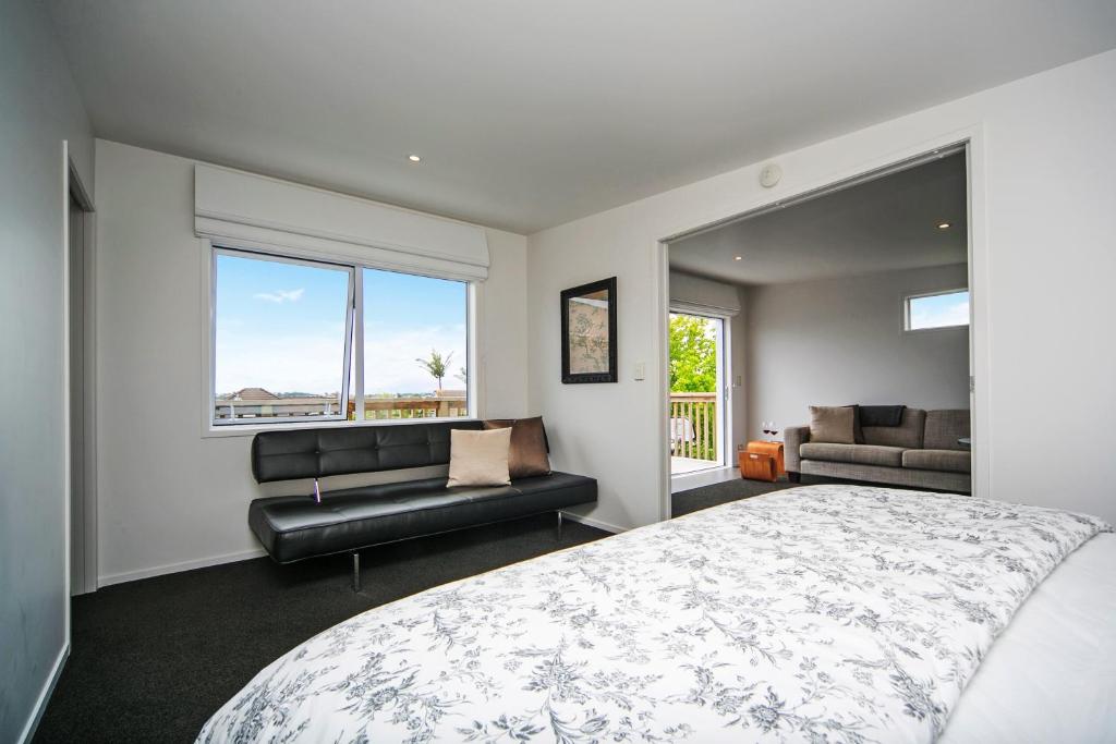 a bedroom with a bed and a couch and windows at Kohi Beach Bed & Breakfast in Auckland
