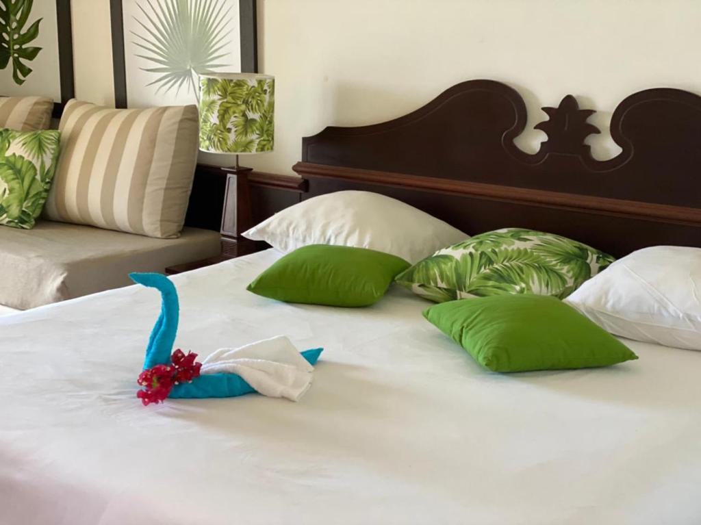 a white bed with green pillows and a toy on it at Studio Charme Créole Accès Plage in Sainte-Luce