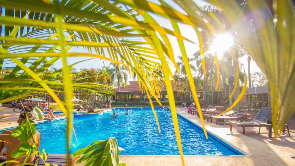 a swimming pool with palm trees and people in it at Complejo Americano in Puerto Iguazú