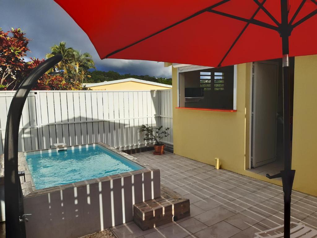 a pool with a red umbrella next to a house at VILLA LINEDDY/ZINNIA in Quartier la Fleury Guiné