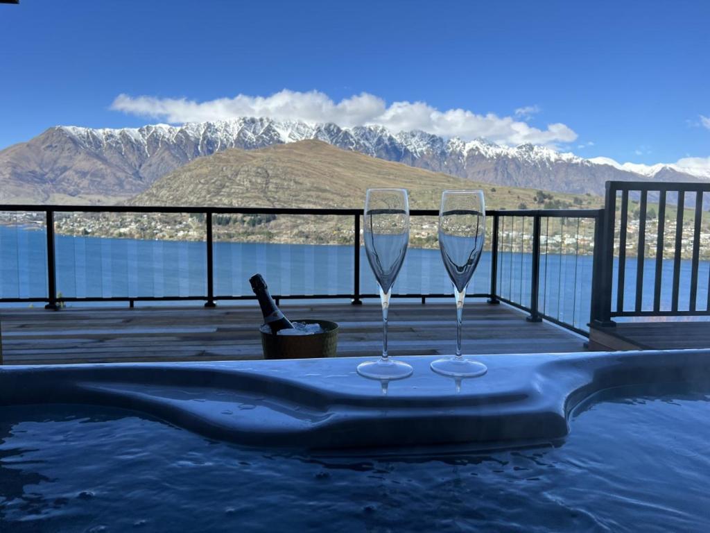 two wine glasses sitting on a table next to a swimming pool at Spa, Mountains & Lake in Queenstown