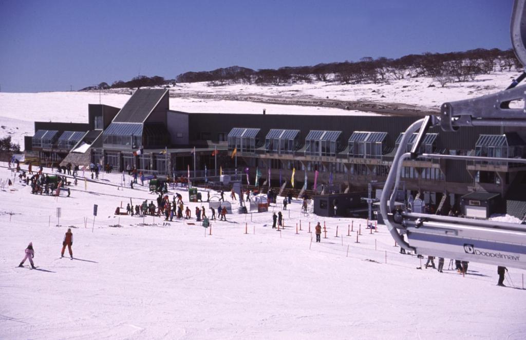 a group of people in the snow in front of a ski lodge at The Perisher Valley Hotel in Perisher Valley