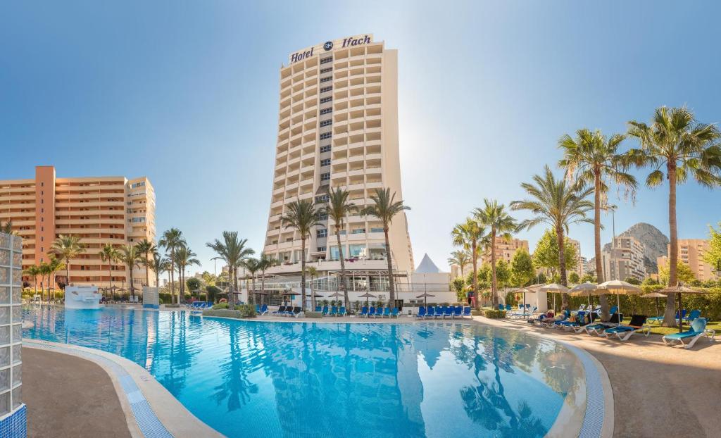 a large swimming pool with palm trees and buildings at Hotel RH Ifach in Calpe