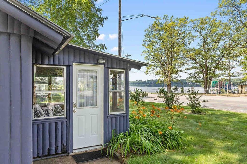 una pequeña casa con una puerta blanca y algunas flores en Cozy pet friendly cabin with dock, firepit, bikes, grill, en Newaygo