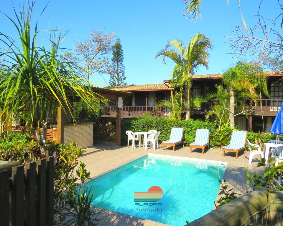 uma piscina com cadeiras e uma mesa e uma casa em Pousada Aurora na Praia do Rosa