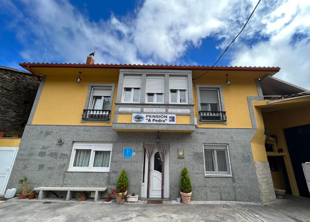 um edifício amarelo e cinzento com um sinal nele em Pensión A Pedra em Dumbría