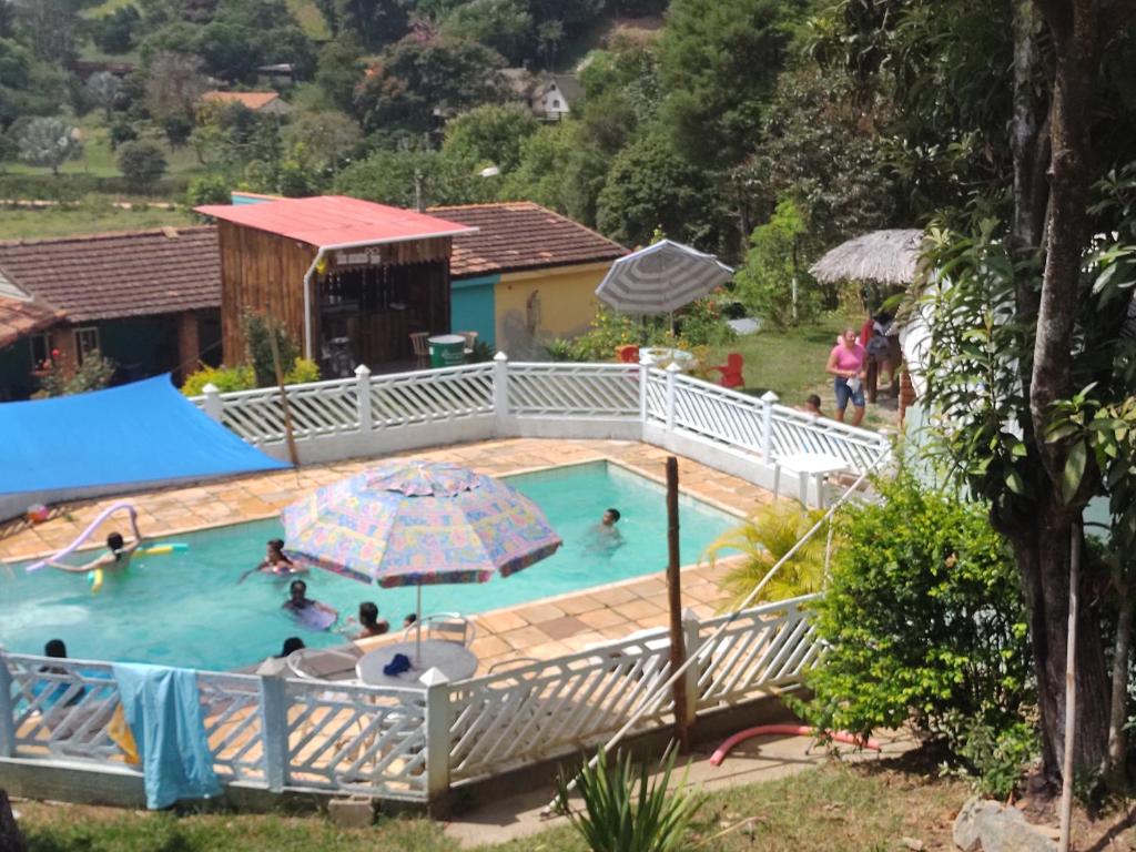un grupo de personas en una piscina con sombrilla en Pousada & Camping Recanto dos Anjos Azuis, en Paty do Alferes
