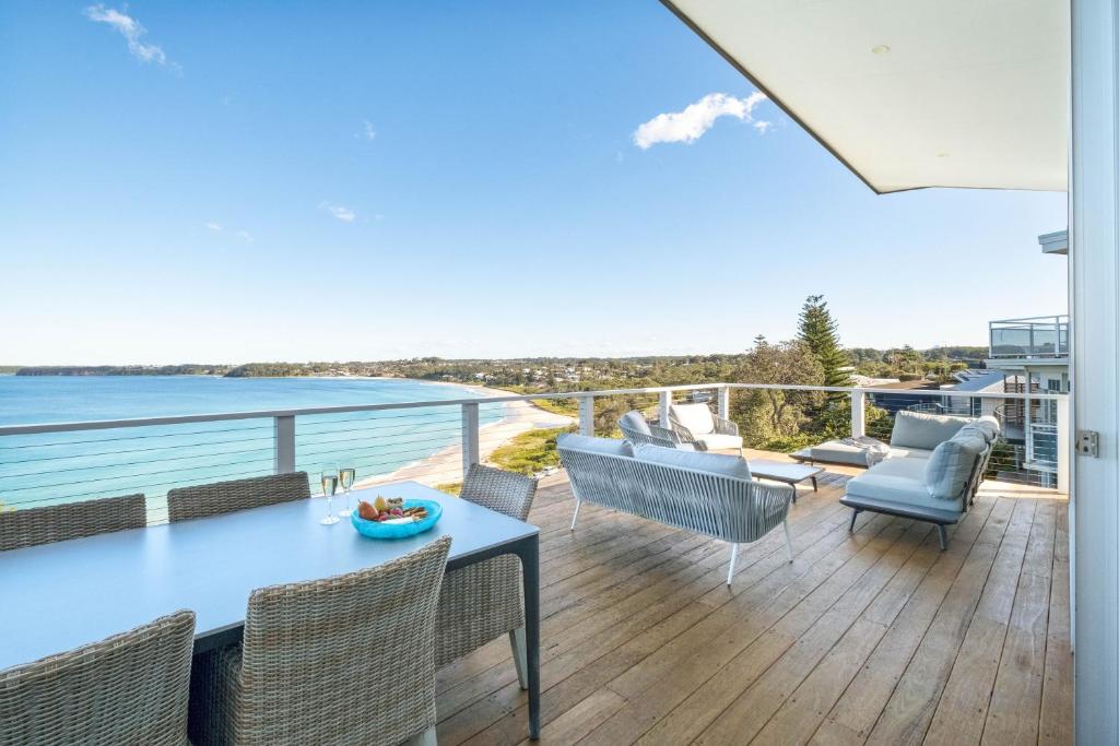 a patio with a table and chairs and the ocean at The Sands Mollymook Luxury Beach House in Mollymook