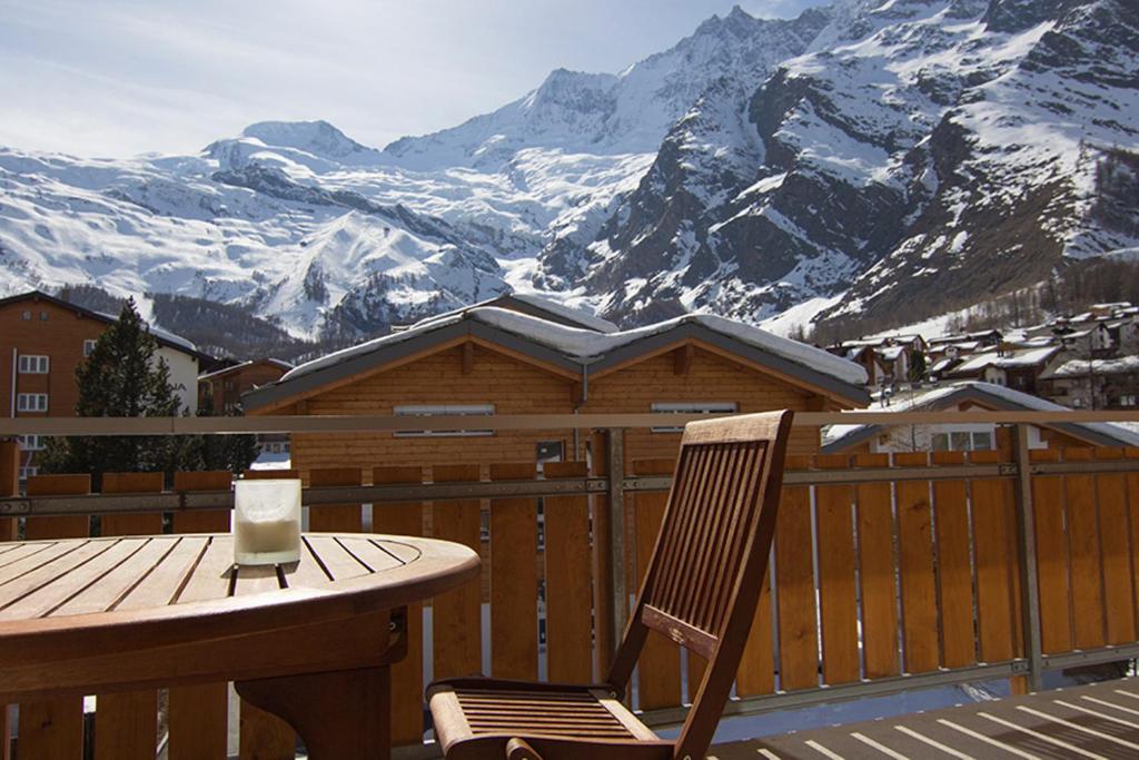 una mesa de madera y una silla en un balcón con montañas en Chalet Haus Perla, en Saas-Fee