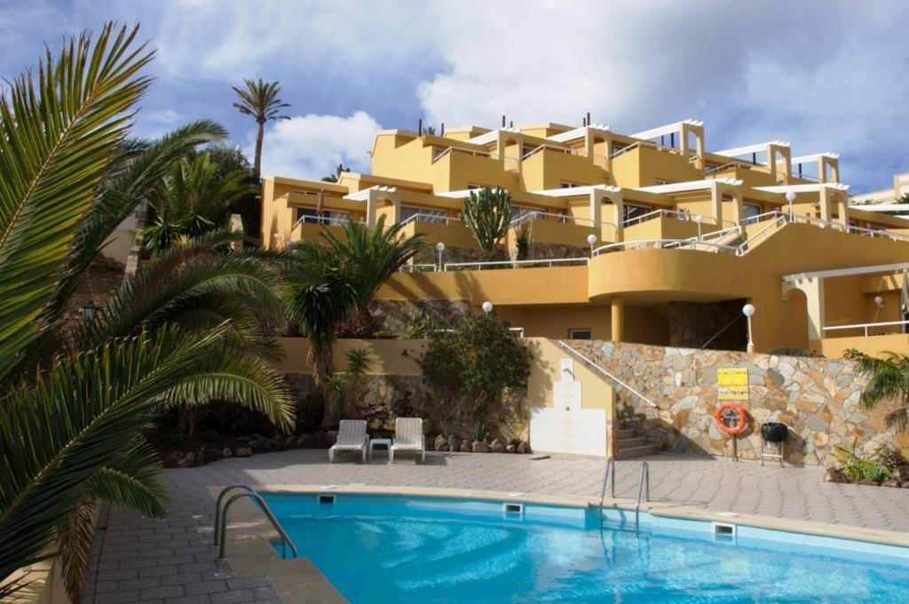 a large yellow building with a swimming pool and palm trees at Apartamentos Punta Marina by LIVVO in Morro del Jable