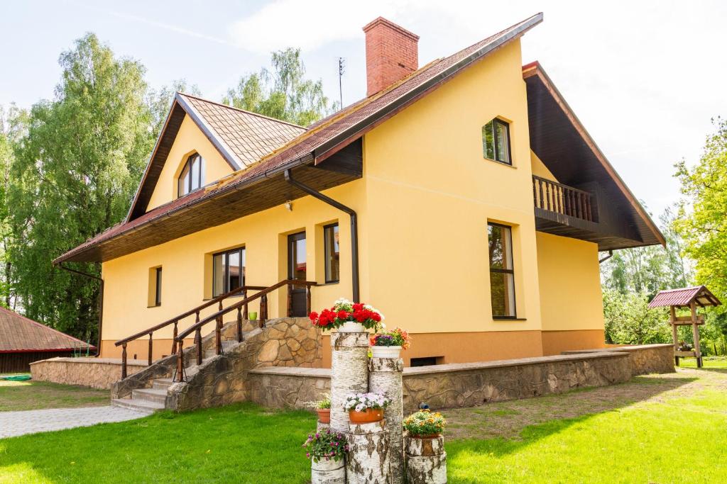 a yellow house with flowers on a tree stump at Viesu nams Sidrabi in Druva