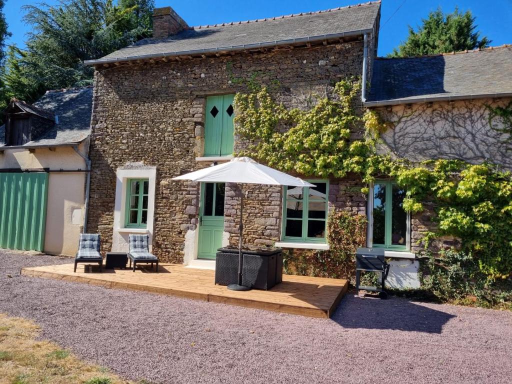 a stone house with an umbrella and two chairs at Longère indépendante avec terrain de tennis privé in Saint-Maugan